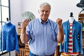 Canvas Print - Senior man with grey hair holding dollars banknotes at retail shop screaming proud, celebrating victory and success very excited with raised arms