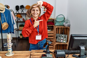 Poster - Middle age blonde woman working working as manager at retail boutique smiling making frame with hands and fingers with happy face. creativity and photography concept.