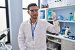 © Krakenimages.com - Young hispanic man with beard working at scientist laboratory holding blue ribbon thinking attitude and sober expression looking self confident