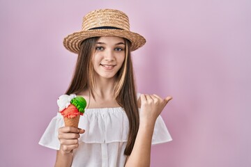 Sticker - Teenager girl holding ice cream pointing to the back behind with hand and thumbs up, smiling confident