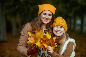 Wall Mural - happy mother and child in hats outdoors in city park in autumn