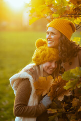 Wall Mural - smiling mom and child in hats outdoors on city park in autumn