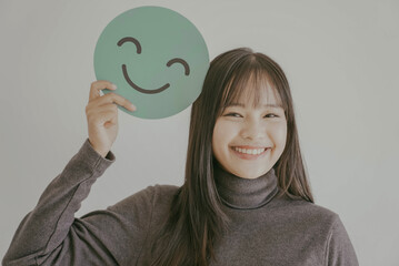 Wall Mural - Happy young Asian woman holding smile emoji face, positive mental health, world mental health day concept
