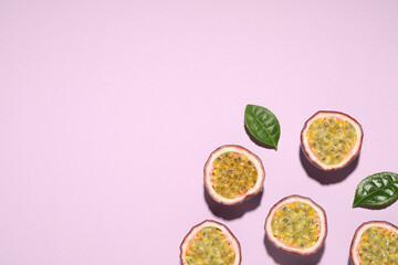 Wall Mural - Halves of passion fruits (maracuyas) and green leaves on pink background, flat lay. Space for text