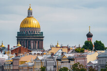 The Huge Golden Dome Of St. Isaac's Cathedral Through The Roofs Of Houses On The Embankment Of The Neva River In St. Petersburg In Cloudy Weather