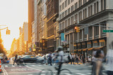 Fototapeta Nowy Jork - Crowds of people walking down the street at a busy intersection on 5th Avenue in New York City with light shining in the background