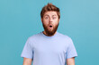 © khosrork - Portrait of shocked bearded man gasps from wonder, holds breath, stares at something horrible keeps mouth opened, being astonished. Indoor studio shot isolated on blue background.