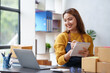 © amnaj - Happy young Asian business owner woman prepare parcel box and check online orders of product for deliver to customer on laptop computer. Shopping Online concept.