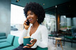 © fotofabrika - Smiling young african woman talking on cellphone at cafe