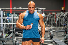 Muscular bodybuilder holding protein bar in gym