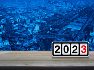 Retro flip clock with 2023 text on wooden table over modern office city tower, street, expressway, and skyscraper, Happy new year 2023 cover concept