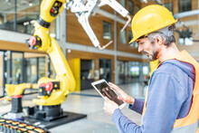 Skilled Worker Controlling Robot Arm With Digital Tablet