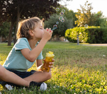 Boy Blowing Bubbles Sitting At Park