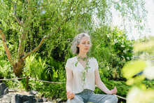 Woman Meditating In Front Of Trees At Park