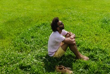 Man Hugging Knees Sitting On Grass In Park