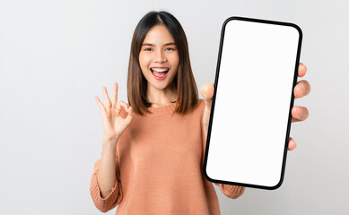 Beautiful Asian woman holding smartphone mockup of blank screen and shows ok sign on grey background
