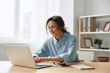 Cheerful adorable curly businesswoman worker freelancer chatting with client registers an order in social media in light office. Happy employee work on computer online in support service. Copy space