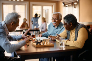 Senior man talks to his friends who are playing chess at nursing home.