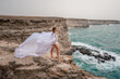 © svetograph - Happy freedom woman on the beach enjoying and posing in white dress over the sea. View of a girl in a fluttering white dress in the wind. Holidays, holidays at sea.