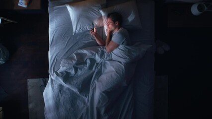 Leinwandbilder - Top View Apartment Bedroom: Handsome Young Man Using Smartphone in Bed at Night. Guy Browsing Through Social Media, Using Dating Apps, Remote Work Software, Internet Online Shopping on Mobile Phone