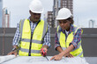 © amorn - African American male engineer and woman engineer worker working with construction building blueprint at construction site. Group of African American construction worker and building blueprint