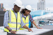 © amorn - African American male engineer worker working with construction model building blueprint at construction site. Group of African American construction worker discussion about building blueprint