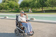 © Renata Hamuda - a smiling woman in an electric wheelchair with disability talks on the phone while enjoying a sunny day stroll in an urban park