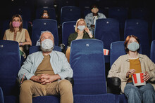 Group Of People Wearing Masks, Keeping Distance From Each Other Watching Movie At Cinema During Quarantine