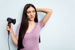 © Asier - Young caucasian woman holding hairdryer isolated on blue background touching back of head, thinking and making a choice.