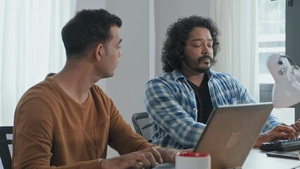Wall Mural - waist up slowmo of two male indian programmers talking while working on computers at desk in office