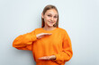 Young caucasian girl isolated on blue background holding something with both hands, product presentation.