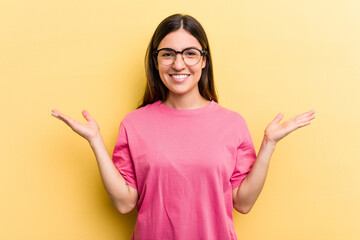 Young caucasian woman isolated on yellow background makes scale with arms, feels happy and confident.