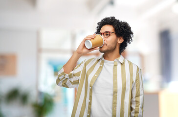 Wall Mural - drinks and people concept - young man in glasses drinking takeaway coffee from paper cup over office background