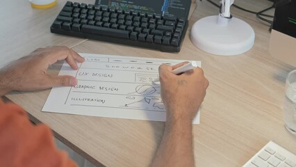 Wall Mural - slowmo of unrecognizable male programmer drawing scheme on sheet of paper while working on computer 