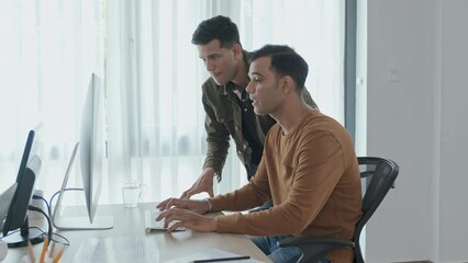 Wall Mural - medium slowmo of two male indian coworkers looking at big computer monitor while discussing corporat