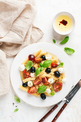 Wall Mural - Cold fussili pasta salad with black olives, mozzarella cheese and cherry tomatoes, top view