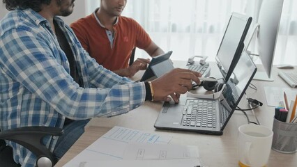 Wall Mural - medium slowmo of two male indian colleagues using laptop and digital tablet while working on corpora
