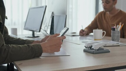 Wall Mural - cropped slowmo of unrecognizable man scrolling on smartphone while sitting at office desk with male 