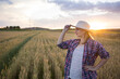 © olga_sova - A beautiful middle-aged farmer woman in a straw hat and a plaid shirt stands in a field of golden ripening wheat during the daytime in the sunlight