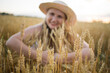 © olga_sova - A beautiful middle-aged farmer woman in a straw hat and a plaid shirt stands in defocus blur a field of golden ripening wheat during the daytime in the sunlight