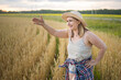 © olga_sova - A beautiful middle-aged farmer woman in a straw hat and a plaid shirt stands in a field of golden ripening wheat during the daytime in the sunlight