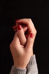 Wall Mural - Female handss in gray knitted sweater with beautiful manicure - red nails on dark black background. Nail care concept