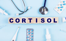On A Blue Background, A Stethoscope, A Thermometer, Other Medicines And Wooden Cubes With The Text CORTISOL. View From Above. Medical Concept