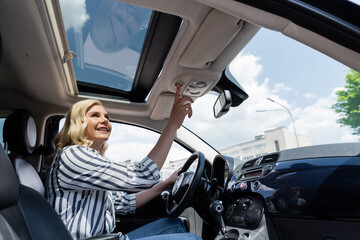 Wall Mural - Positive blonde woman pushing button and looking at top of car