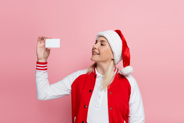Wall Mural - smiling blonde woman in santa hat holding empty driving license isolated on pink