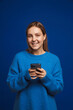 © Drobot Dean - Young handsome girl in blue sweater holding phone and looking in camera