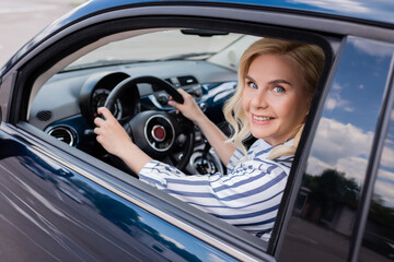 Wall Mural - Blonde woman looking at camera in blurred car during driving course