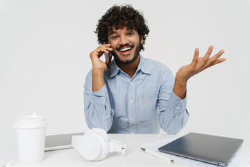 Wall Mural - Young smiling indian man sitting at table talking phone