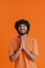 Wall Mural - Young indian curly smiling man with folded hands looking upward