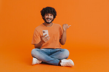 Wall Mural - Young indian smiling man sitting with phone in lotus pose